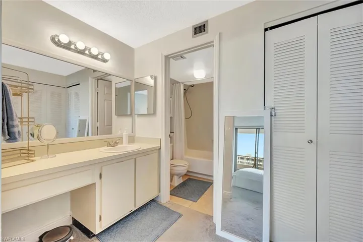 Full bath with a closet, vanity, shower / tub combo with curtain, a textured ceiling, and light tile patterned floors