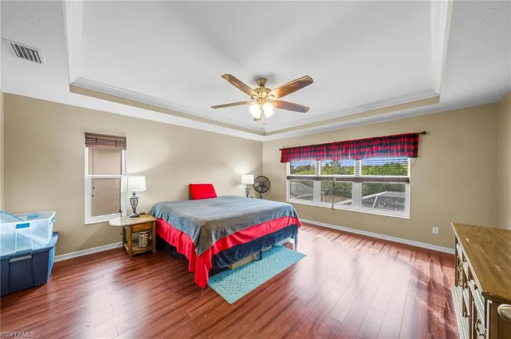 Bedroom featuring a raised ceiling, dark wood finished floors, a ceiling fan, and crown molding