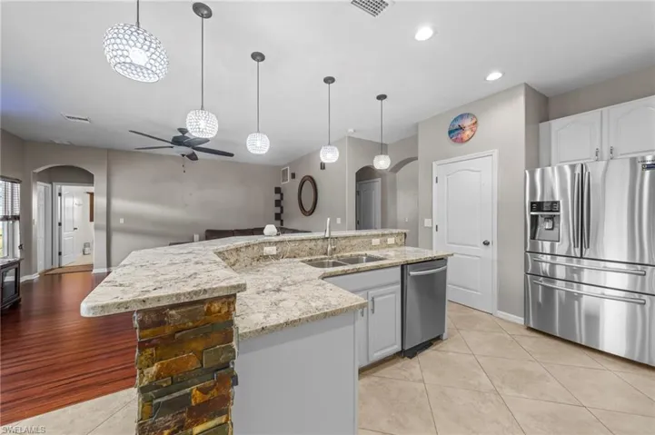 Kitchen featuring arched walkways, ceiling fan, stainless steel appliances, a kitchen island with sink, and recessed lighting