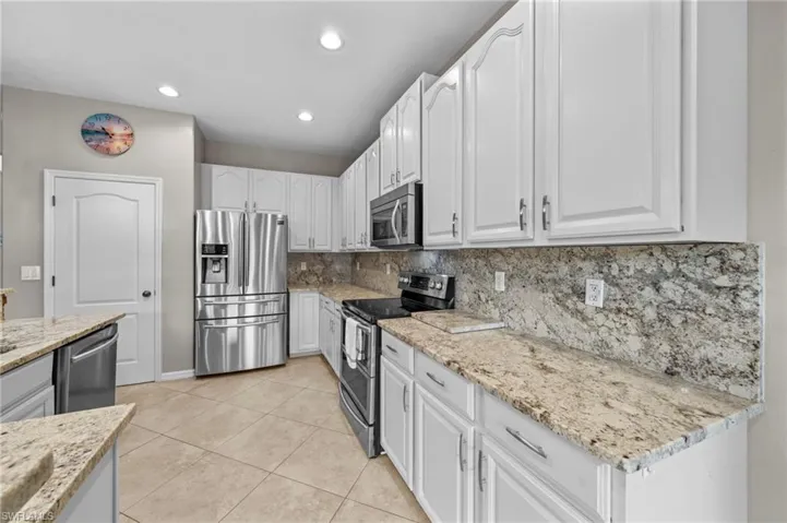 Kitchen featuring stainless steel appliances, white cabinets, light stone counters, backsplash, and light tile patterned floors