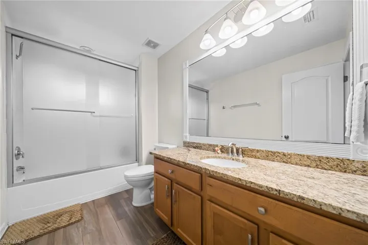 Full bath featuring vanity, dark wood-type flooring, and enclosed tub / shower combo