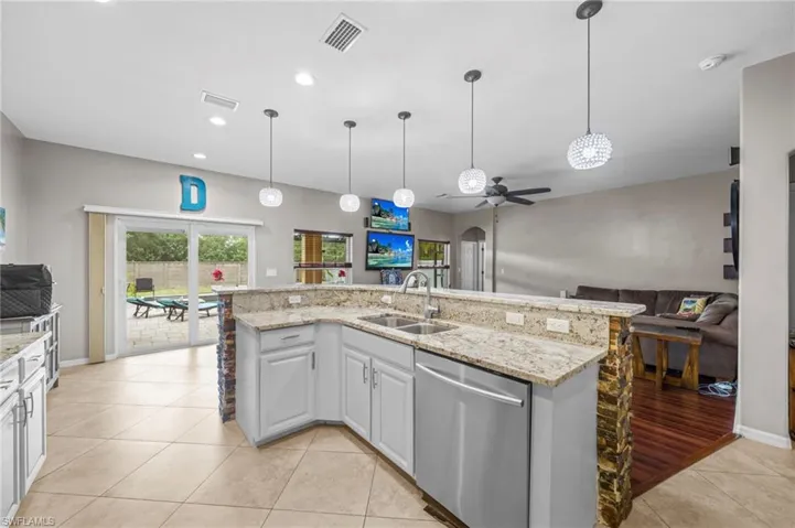 Kitchen with light stone counters, open floor plan, stainless steel dishwasher, hanging light fixtures, and recessed lighting