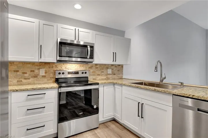 Kitchen with tasteful backsplash, appliances with stainless steel finishes, sink, white cabinetry, and LVT floor