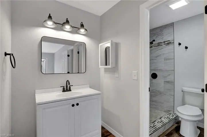 Bathroom featuring toilet, LVT floor, vanity, and tiled shower
