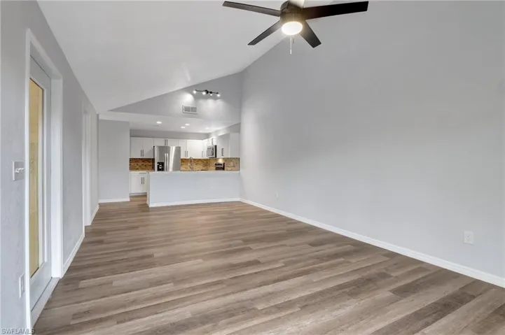 Unfurnished living room with ceiling fan, high vaulted ceiling, and LVT floor