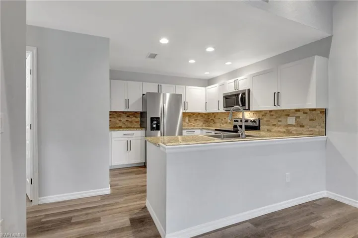 Kitchen featuring appliances with stainless steel finishes, kitchen peninsula, white cabinets, and LVT floor