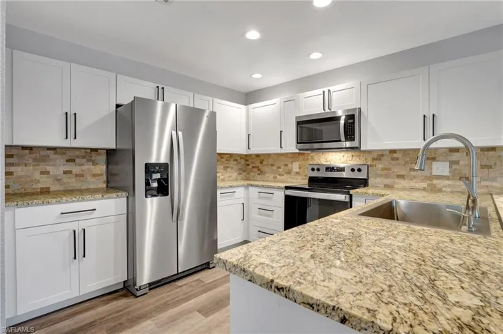 Kitchen with stainless steel appliances, sink, white cabinetry, LVT floor, and tasteful backsplash