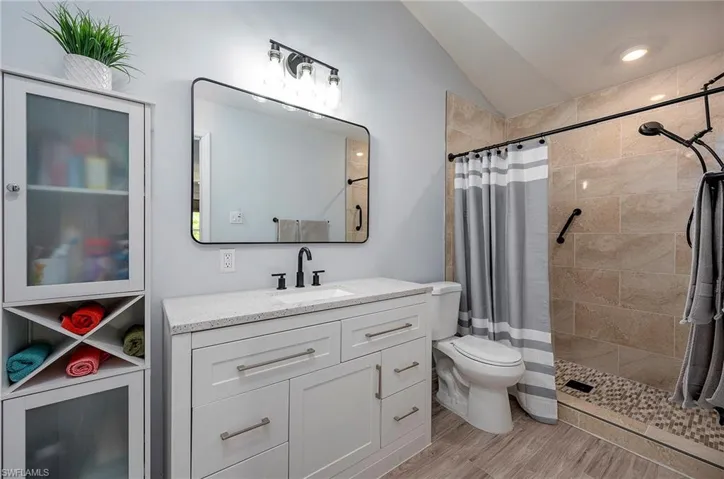 Bathroom featuring oversized vanity, vaulted ceiling, walk in shower, hardwood / wood-style flooring, and toilet
