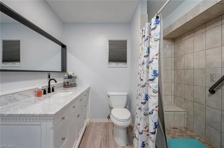 Bathroom featuring curtained shower, hardwood / wood-style floors, toilet, and vanity