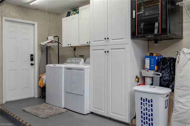 Laundry room with washer and dryer, a textured ceiling, and cabinets