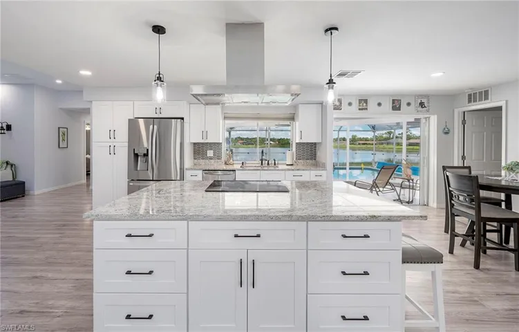 Kitchen featuring light hardwood / wood-style floors, stainless steel fridge, island range hood, white cabinets, and backsplash