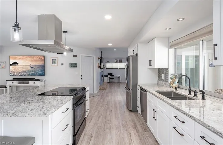 Kitchen with island exhaust hood, stainless steel appliances, light wood-type flooring, hanging light fixtures, and sink