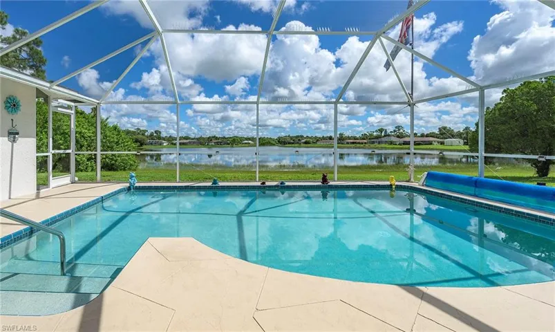 View of swimming pool with a patio area, glass enclosure, and a water view