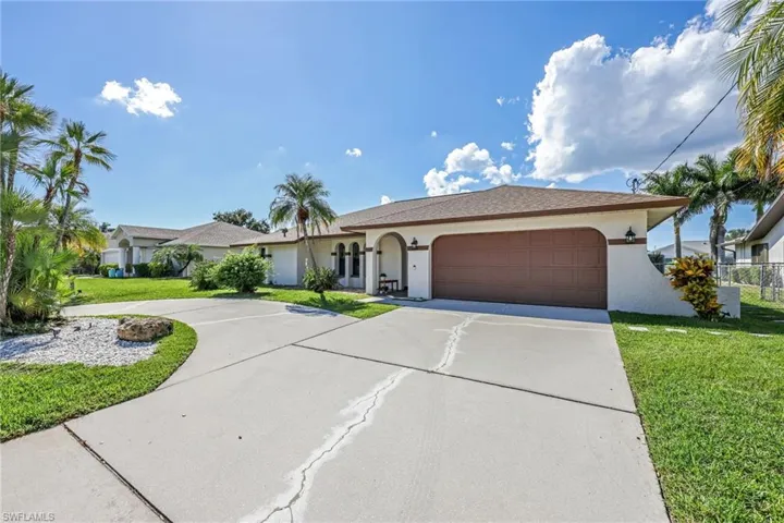 Single story home featuring a front lawn, driveway, stucco siding, and an attached garage