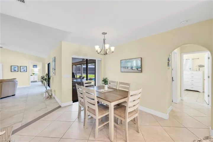 Dining space with light tile patterned floors, arched walkways, a chandelier, and vaulted ceiling