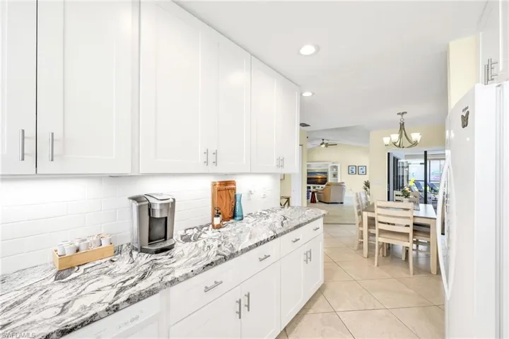 Kitchen with white cabinets, freestanding refrigerator, decorative backsplash, light stone countertops, and recessed lighting