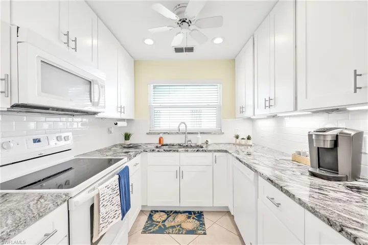 Kitchen with white appliances, white cabinetry, light tile patterned floors, recessed lighting, and light stone counters
