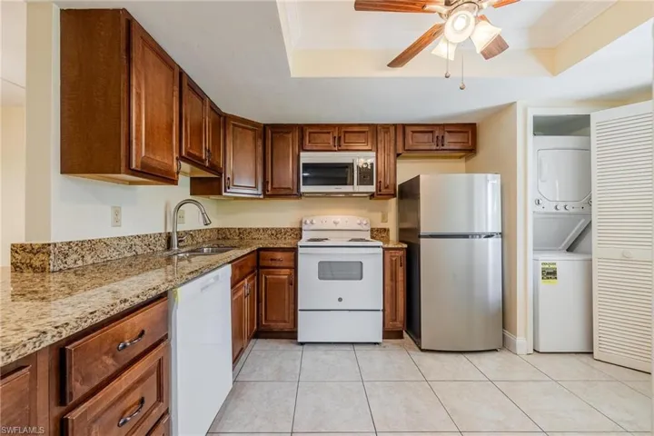 Kitchen with granite counters, dark wood cabinets, stacked washer / dryer, crown molding, and a tray ceiling
