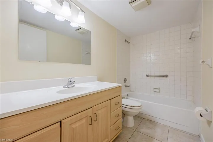 Full bathroom with vanity, tiled shower / bath combo, toilet, and tile patterned floors