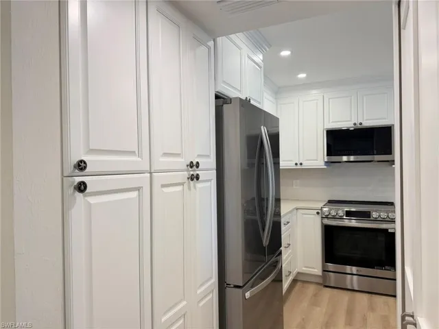 Kitchen with stainless steel appliances, white cabinetry, recessed lighting, light wood finished floors, and crown molding