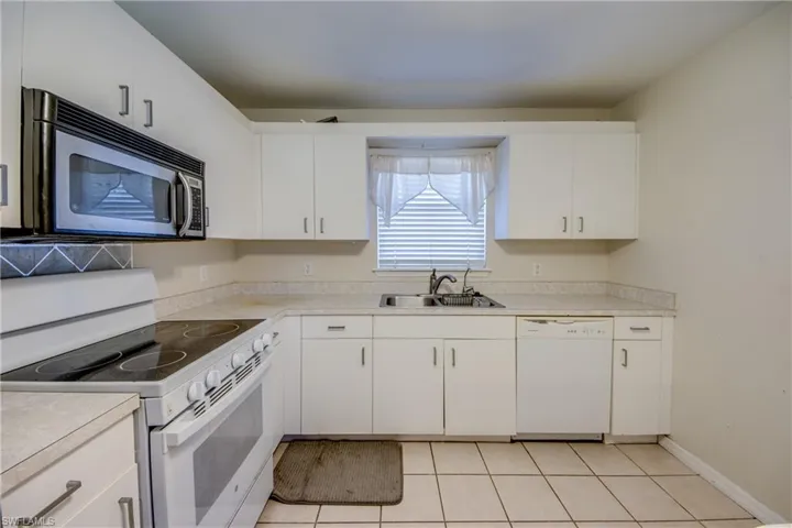 Kitchen with white appliances, light countertops, white cabinets, and light tile patterned flooring