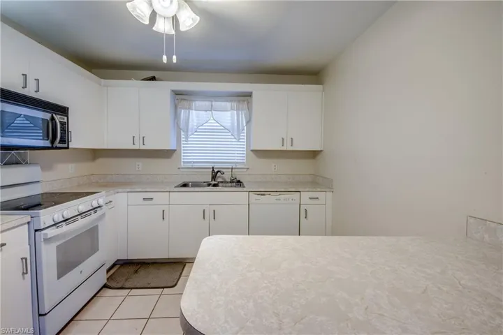 Kitchen featuring white appliances, light countertops, white cabinets, and light tile patterned floors