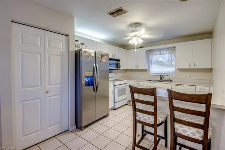 Kitchen with stainless steel appliances, a kitchen breakfast bar, light countertops, ceiling fan, and white cabinets