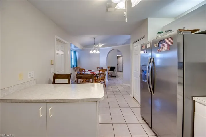 Kitchen featuring stainless steel refrigerator with ice dispenser, light tile patterned flooring, light countertops, a peninsula, and arched walkways