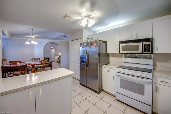 Kitchen featuring stainless steel appliances, light countertops, ceiling fan, white cabinetry, and arched walkways