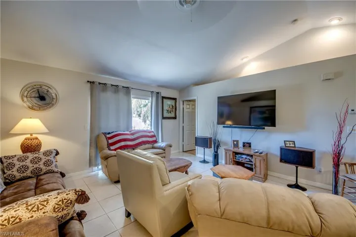 Living room with lofted ceiling, tile patterned flooring, and a ceiling fan