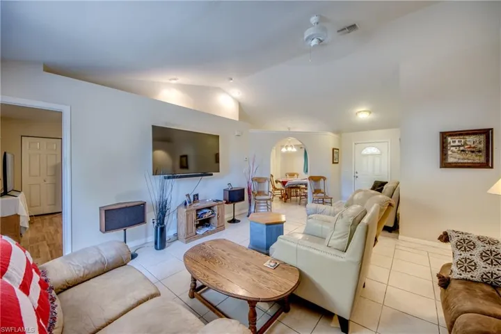 Living room with vaulted ceiling, light tile patterned floors, suspended lighting, arched walkways, and ceiling fan