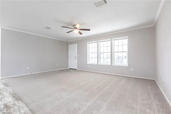Empty room featuring light colored carpet, ceiling fan, and crown molding