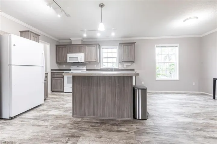 Kitchen with white appliances, crown molding, light wood-style flooring, a kitchen island, and light countertops