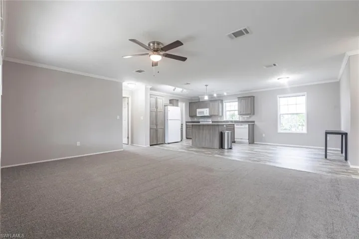 Unfurnished living room featuring ornamental molding, light colored carpet, and ceiling fan