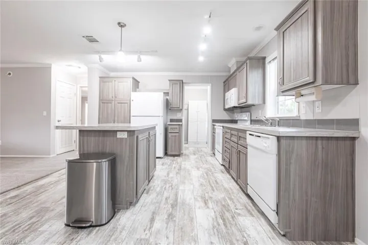 Kitchen with crown molding, white appliances, light countertops, rail lighting, and light wood-style flooring