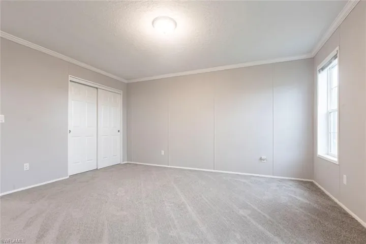 Unfurnished bedroom featuring carpet floors, a textured ceiling, a closet, crown molding, and a decorative wall