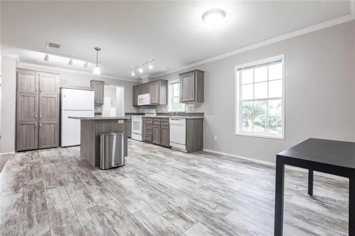 Kitchen featuring ornamental molding, white appliances, a center island, decorative light fixtures, and light wood-type flooring