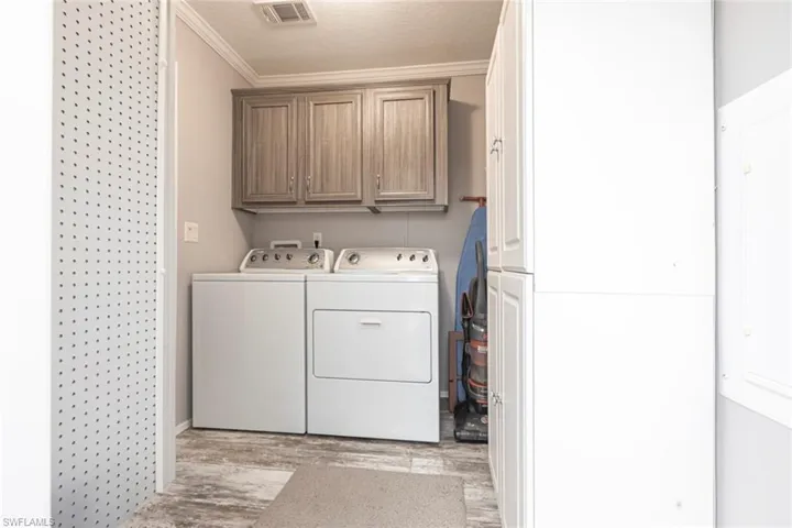Laundry area featuring cabinet space, light wood-style floors, washing machine and clothes dryer, ornamental molding, and a textured ceiling