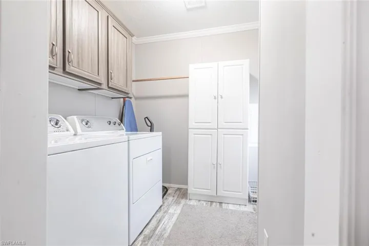 Laundry room with cabinet space, washer and clothes dryer, light wood finished floors, and crown molding