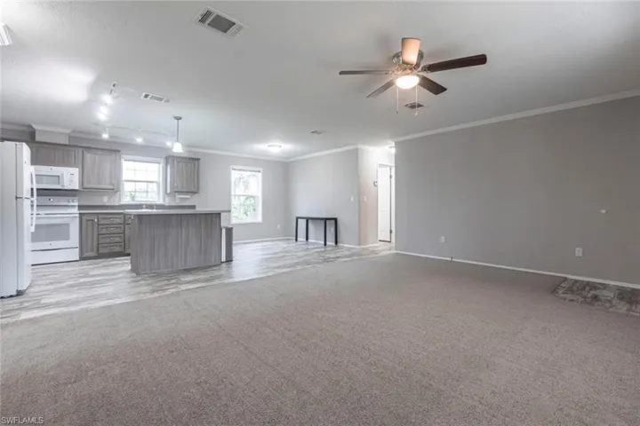 Kitchen featuring open floor plan, white appliances, light colored carpet, a ceiling fan, and crown molding