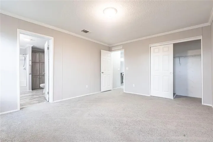 Unfurnished bedroom featuring light colored carpet, ornamental molding, a closet, connected bathroom, and a textured ceiling