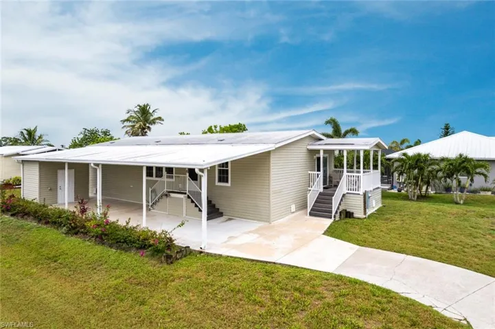 View of front facade featuring a front yard, an attached carport, driveway, and a metal roof