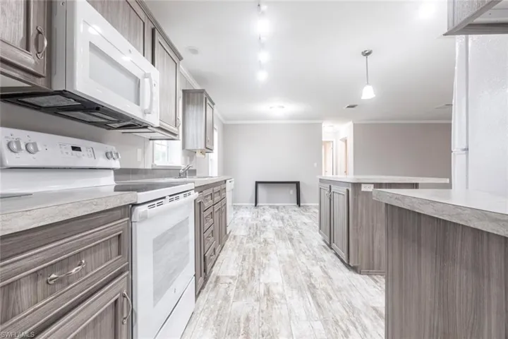 Kitchen featuring white appliances, ornamental molding, light countertops, light wood-style flooring, and pendant lighting