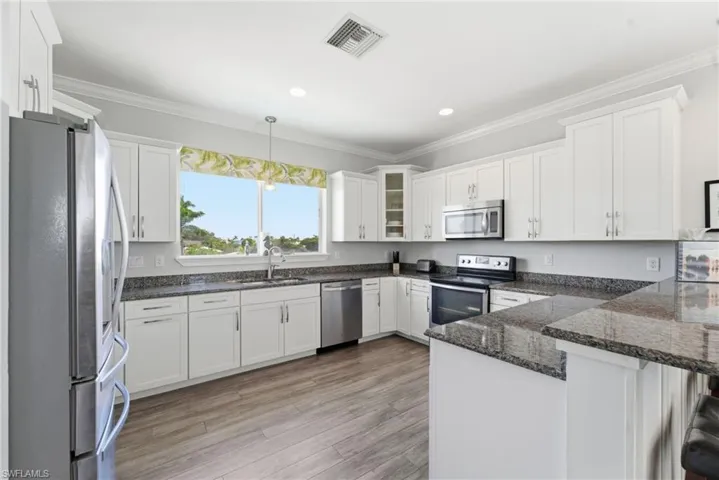 Kitchen with white cabinets, ornamental molding, stainless steel appliances, dark stone counters, and light wood-style floors