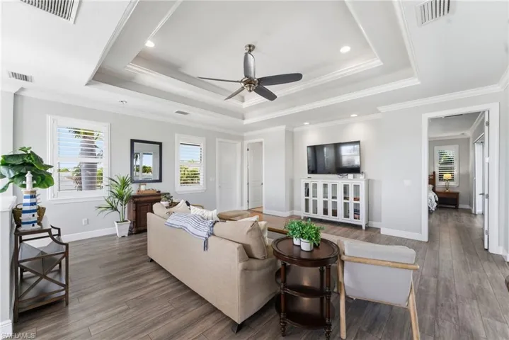 Living area with healthy amount of natural light, a raised ceiling, ceiling fan, ornamental molding, and wood finished floors