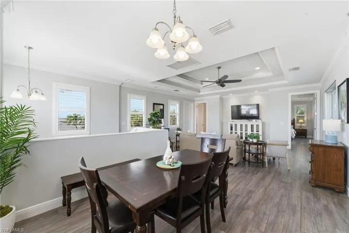 Dining area with a chandelier, ornamental molding, a tray ceiling, wood finished floors, and ceiling fan