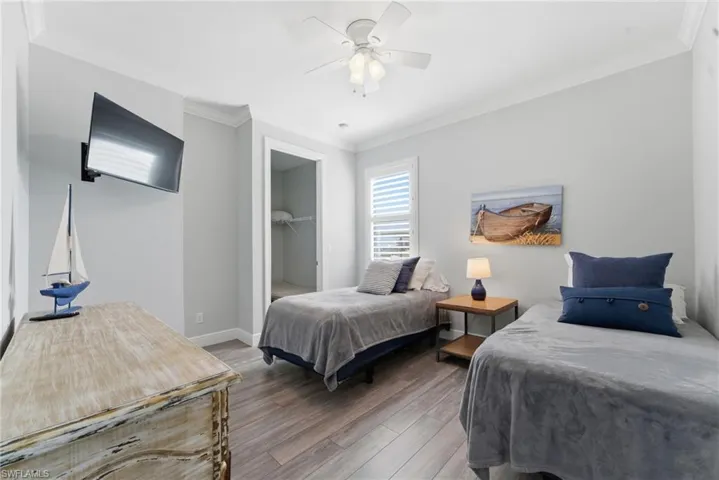 Bedroom featuring crown molding, a spacious closet, wood finished floors, and a ceiling fan