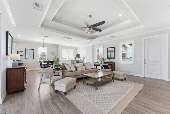 Living area with a raised ceiling, crown molding, a ceiling fan, light wood-type flooring, and a chandelier