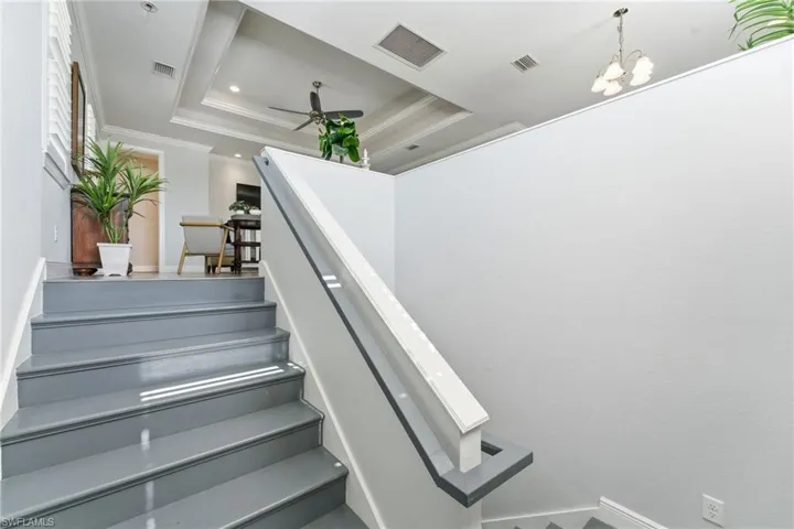 Stairs featuring a raised ceiling, ornamental molding, a ceiling fan, a chandelier, and recessed lighting