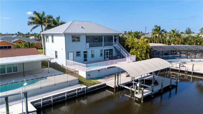 Back of property featuring an outdoor pool, boat lift, a patio area, a fenced backyard, and a water view